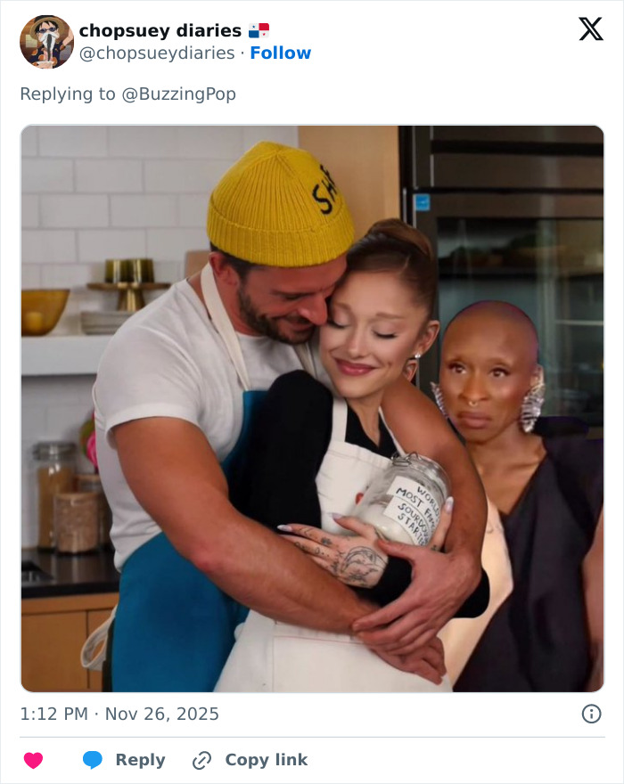 Ariana Grande and Jonathan Bailey sharing an intimate moment in a kitchen while another person looks on.