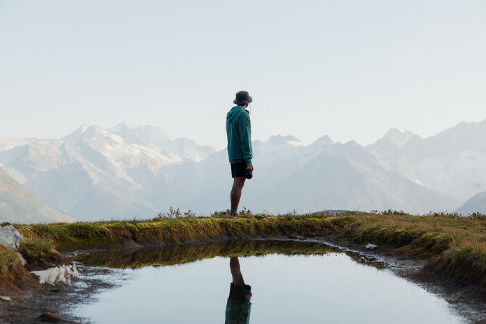 Person standing near a mountain lake reflecting snowy peaks, symbolizing a journey to find purpose and direction.