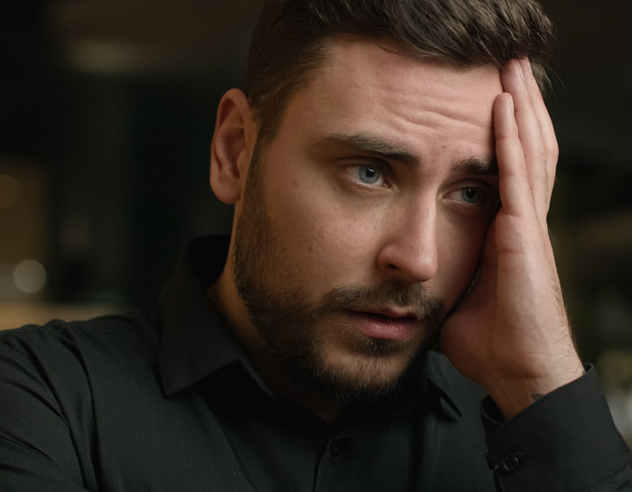 Young man looking stressed and conflicted, illustrating a mother-in-law and son choosing wife and baby over her tension.