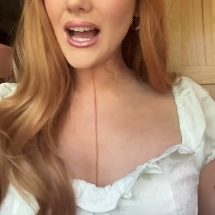 Tattoo artist discussing tattoo regrets while showing a fresh tattoo line on her chest in a casual indoor setting.