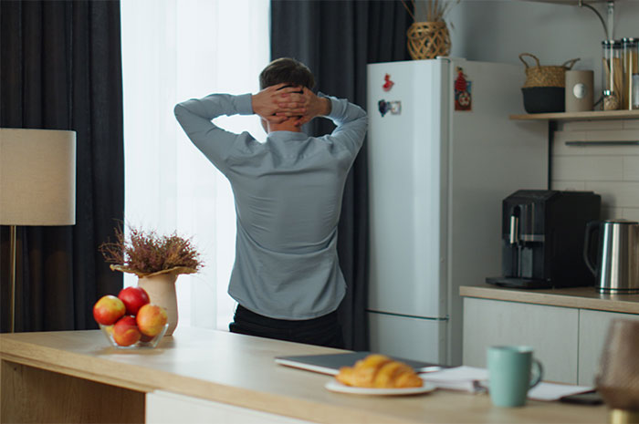 Man stressed in kitchen, standing with hands on head, frustrated after girlfriend ate all the leftovers causing weight gain concerns.