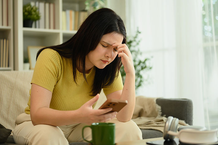 Woman looking distressed while using a smartphone, representing MIL plays the victim in family cutting contact with gay couple.