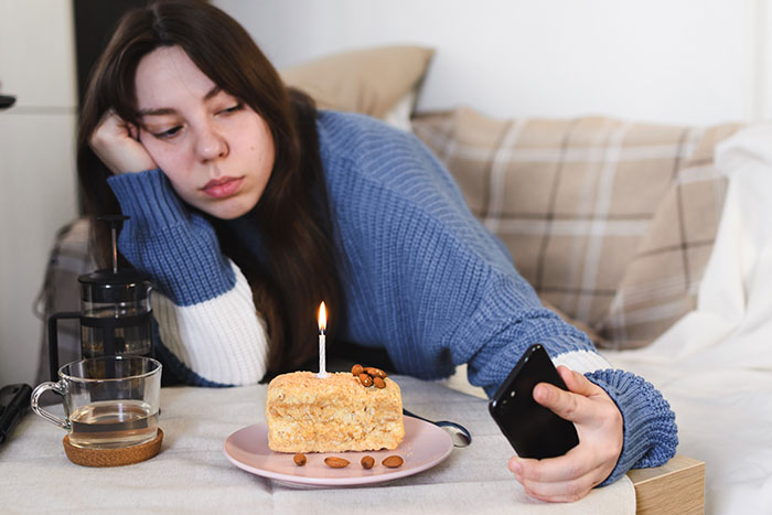 Sad woman in a blue sweater taking a selfie with a small birthday cake and single candle on the table during holidays. Sad woman in a blue sweater taking a selfie with a small birthday cake and single candle on the table during holidays.