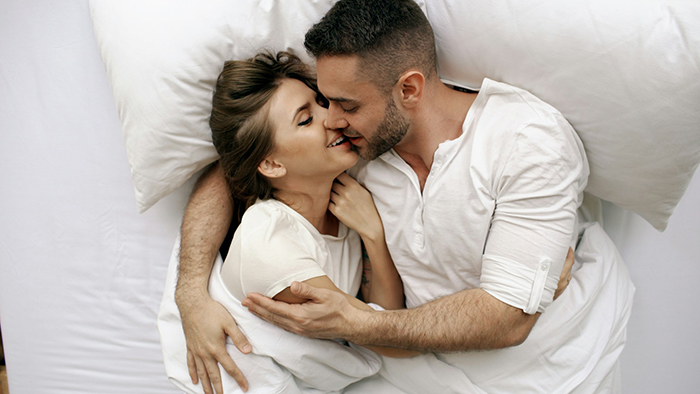 Man and woman embracing intimately in bed, symbolizing complex relationship dynamics while working things out.