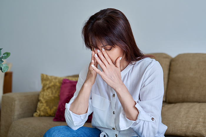 Woman sitting on couch, distressed and covering her face, reflecting on inspiring 5 year update after leaving cheating husband. Woman sitting on couch, distressed and covering her face, reflecting on inspiring 5 year update after leaving cheating husband.