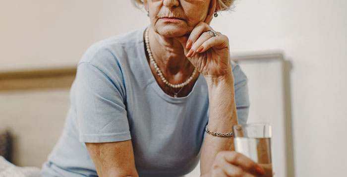 Elderly woman in a blue shirt looking thoughtful while holding a glass, reflecting the theme of family drama stories.