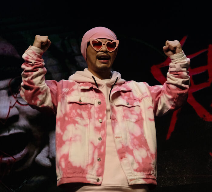 Man wearing pink tie-dye jacket and heart-shaped sunglasses raising fists, linked to provocative influencer found in hotel bathtub. Man wearing pink tie-dye jacket and heart-shaped sunglasses raising fists, linked to provocative influencer found in hotel bathtub.