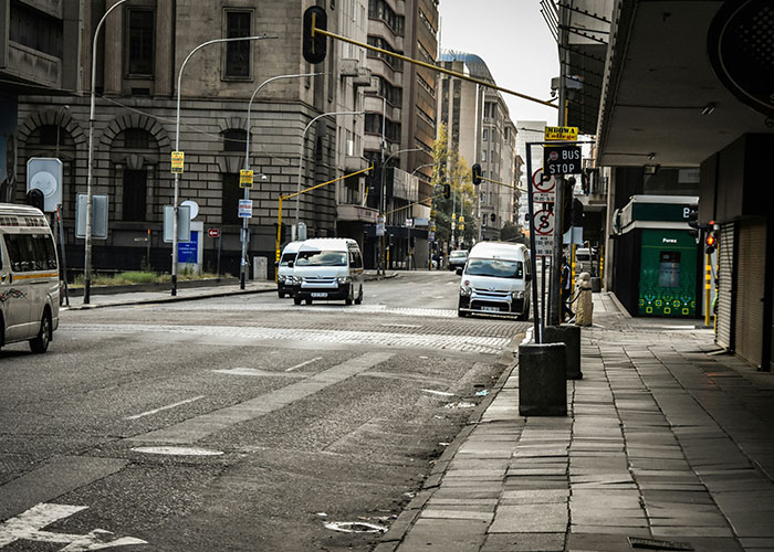 Deserted urban street in one of the worst cities worldwide, showing empty sidewalks and sparse traffic at a bus stop.