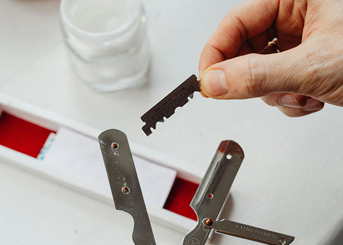 Hand holding a razor blade found inside the walls of a home, alongside metal tools on a white surface.