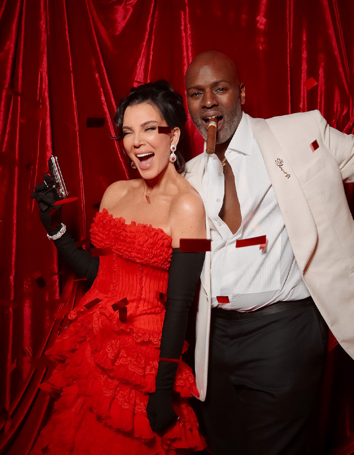 Guests at Kris Jenner's 70th birthday bash pose in elegant attire amid red confetti and dramatic red backdrop.