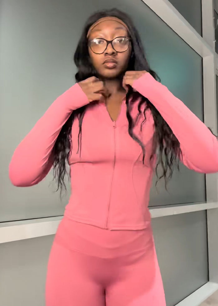 Young woman wearing pink activewear demonstrating trick to hide loose skin on her belly after massive weight loss indoors.