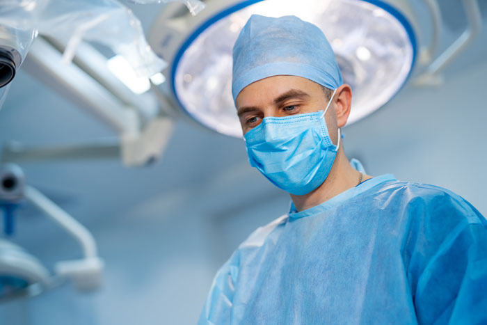 Surgeon in blue scrubs and mask working under an operating room light illustrating funny patients’ comments in hospitals.