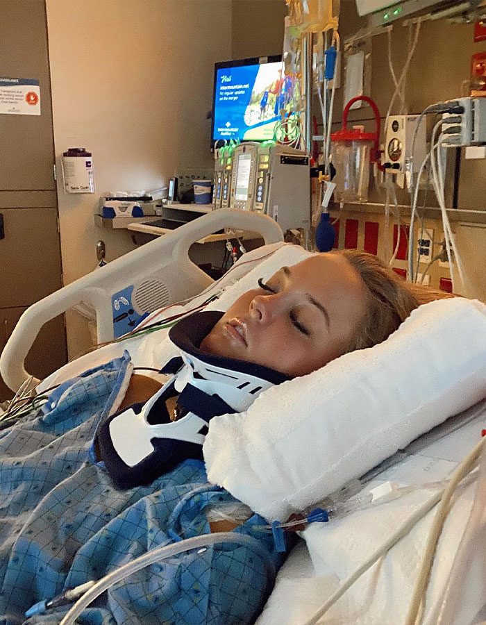 Young girl who was paralyzed at 16 lying in a hospital bed wearing a neck brace and connected to medical devices.