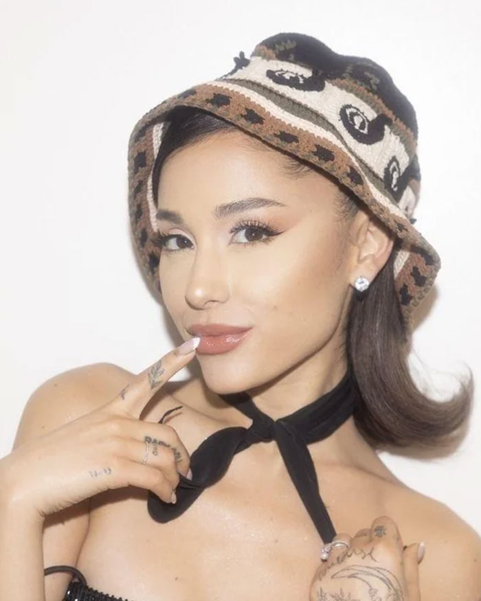 Ariana Grande posing with a patterned bucket hat and black neck scarf, fans discuss possible plastic surgery changes.