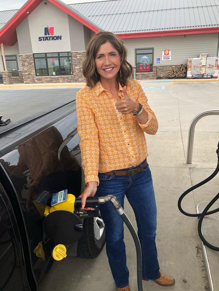 Kristi Noem smiling while pumping gas at a station, wearing a yellow patterned shirt and blue jeans outdoors. Kristi Noem smiling while pumping gas at a station, wearing a yellow patterned shirt and blue jeans outdoors.