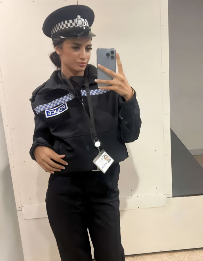 Female trainee police officer in uniform taking a mirror selfie with badge and cap in an indoor setting. Female trainee police officer in uniform taking a mirror selfie with badge and cap in an indoor setting.
