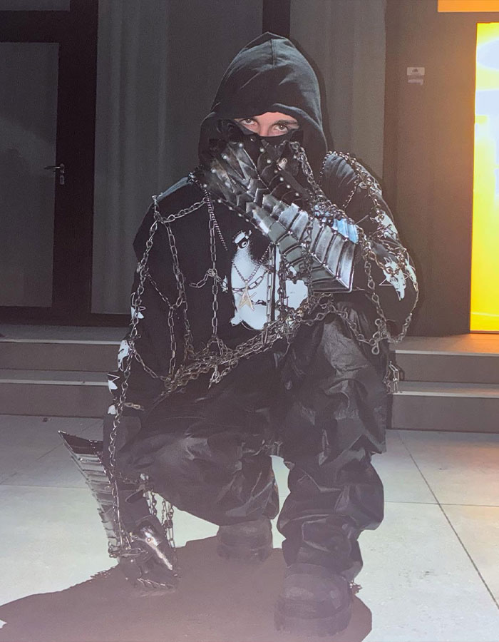 Person in a hooded outfit with chains and metallic gloves posing, fueling fans' theory of Timoth&eacute;e Chalamet as rapper EsDeeKid.