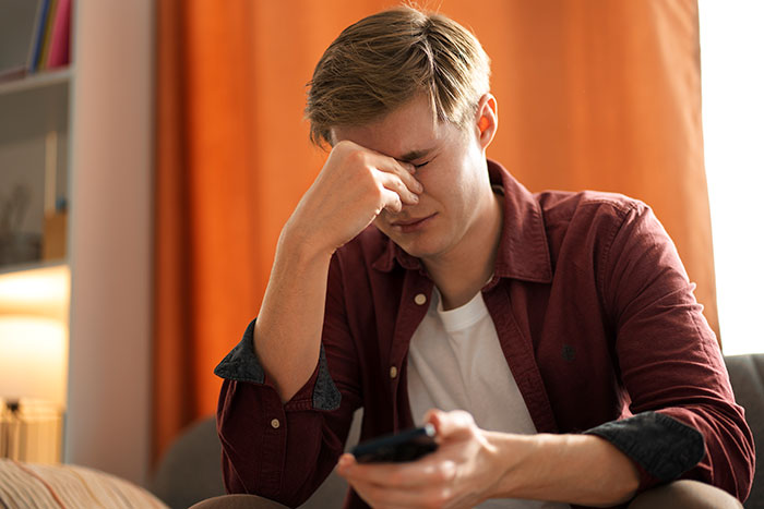 Young man stressed and holding his forehead while sitting indoors, representing entitled parents and autistic brother issues.