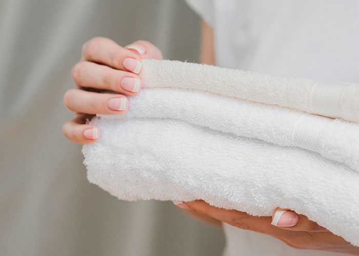 Hand holding neatly folded white towels demonstrating genius cleaning hacks inspired by laziness for easy home care.