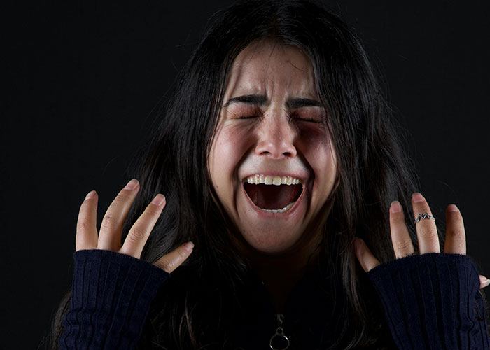 Woman with disheveled hair wearing dark clothing, expressing intense emotion, illustrating psychiatric institution worker experiences.
