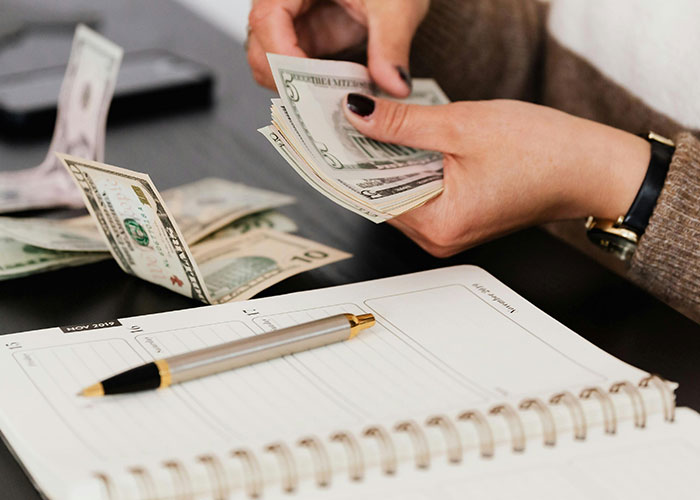 Person counting cash with a planner and pen nearby, illustrating practical life hacks for better money management.