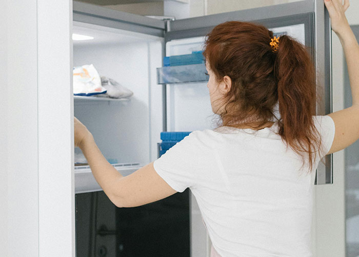 Woman with red hair organizing items in an open refrigerator, demonstrating genius cleaning hacks inspired by laziness.