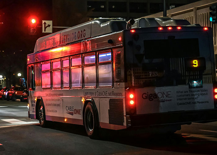 Nighttime urban street scene with a city bus illuminated by red and purple lights, evoking bizarre events atmosphere.