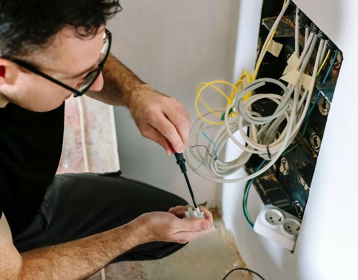 Man working on wiring with a screwdriver near an open electrical panel, illustrating people who messed up once and learned.