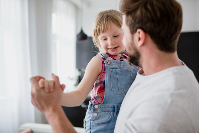 Man holding and playing with a young girl indoors, highlighting parenting challenges with kids every weekend.