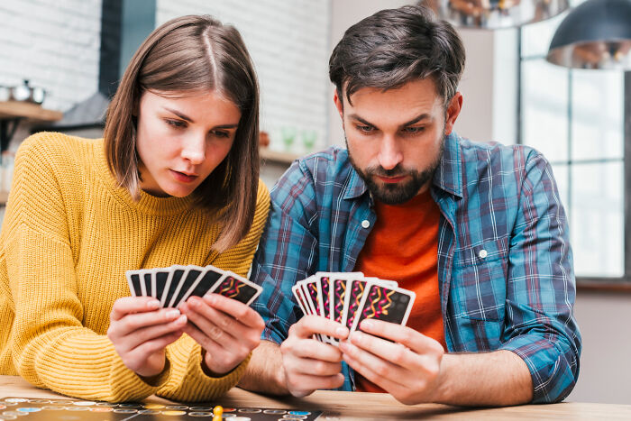 Two people focused on playing a card game, illustrating Thanksgiving arguments and family tensions during holiday gatherings.