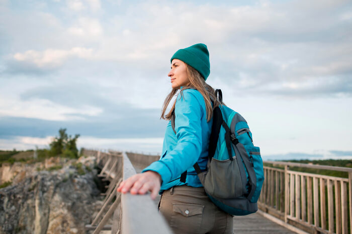 Young woman with backpack standing on a bridge looking into the distance, symbolizing people who disappeared to start new lives.