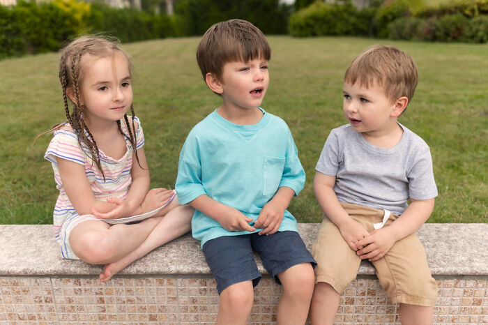Three kids sitting outdoors, engaging in a candid moment that shows weird behaviors passed down from parents.