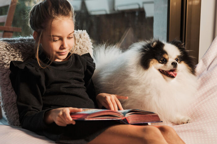 Young girl reading a book next to her fluffy dog, showcasing the most insane dog mom things in a cozy setting.