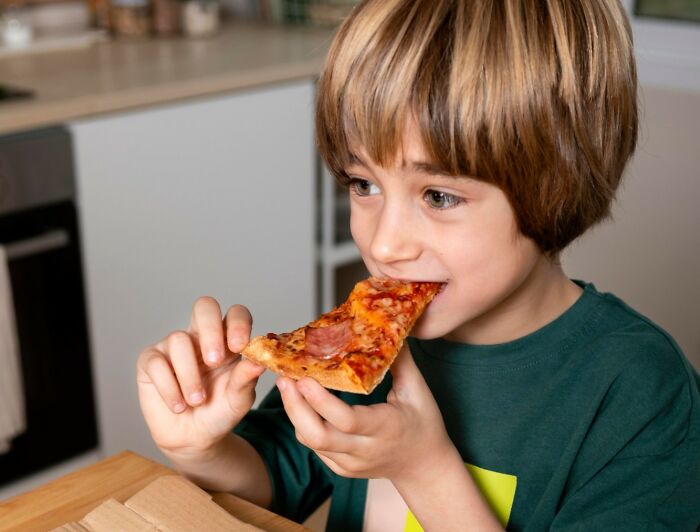 Young child eating pizza at home, illustrating relatable moments for nepo babies sharing insider experiences.