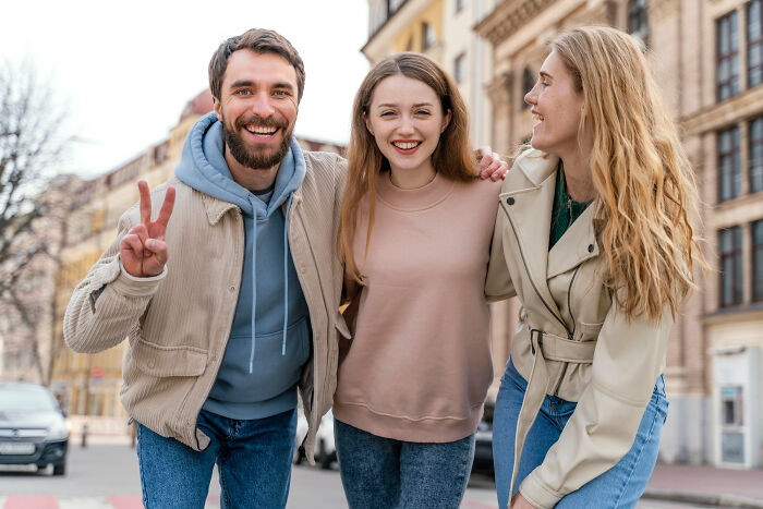 Three friends smiling outdoors with a focus on uneasy feelings about sleeping arrangements in hosting a newly single friend