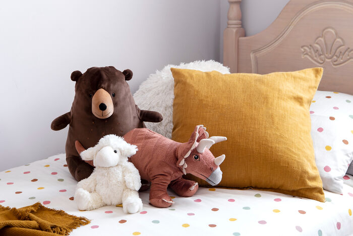 Stuffed bear, dinosaur, and sheep toys on a polka dot bed with a mustard pillow, illustrating little lie storytelling concept.