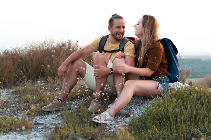 Young couple sitting outdoors on a hillside, smiling and enjoying nature, symbolizing people who disappeared to start new lives.