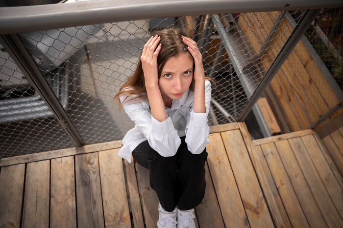 Teenage girl sitting alone on wooden floor, holding head with hands, showing signs child never loved properly.