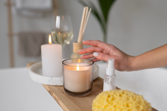 Hand reaching for a lit candle on a wooden bathtub tray, symbolizing calm during Thanksgiving arguments online.