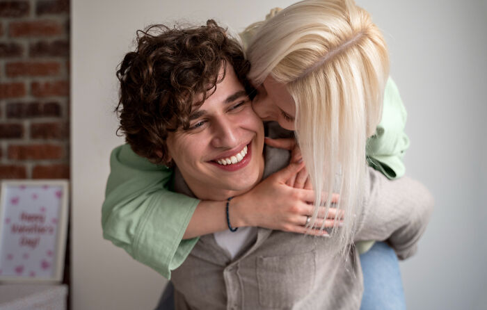 Young woman hugging a smiling man from behind, showing signs of a child feeling loved and cared for properly.