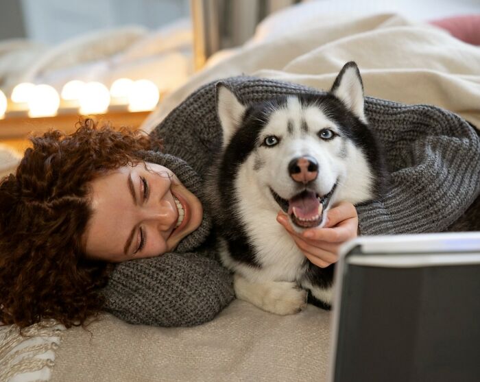 A happy dog mom lying on bed, smiling and cuddling her husky, capturing most insane dog mom things with her pet.