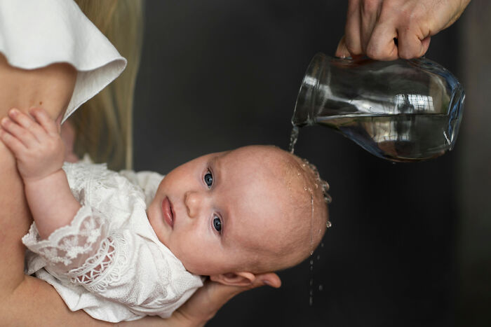 Infant held by adult while water is poured over head, illustrating stories of folks realizing compulsory things in life were optional.