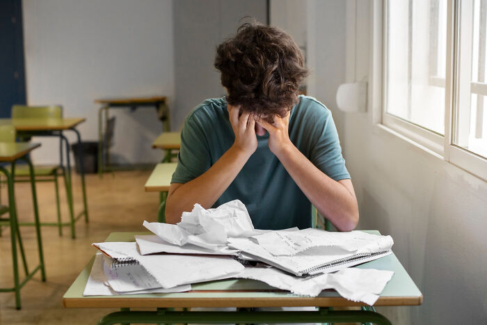 Teen boy stressed over schoolwork, sitting at desk with crumpled papers, representing little lie that backfired on them hard.