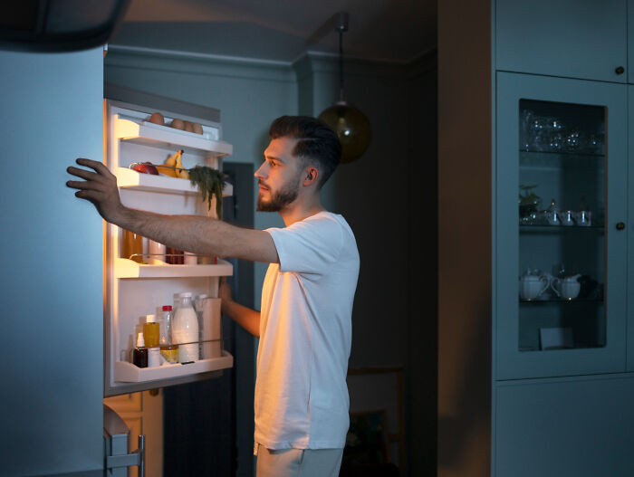 Man opening refrigerator at night, reflecting on childhood habits that were anything but normal.