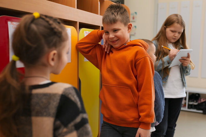 Children in a school hallway, one boy in an orange hoodie talking to a girl, illustrating little lie backfired moments.
