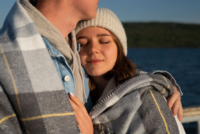 Young woman wrapped in a blanket with a man outdoors by the water, reflecting signs a child was never loved properly.