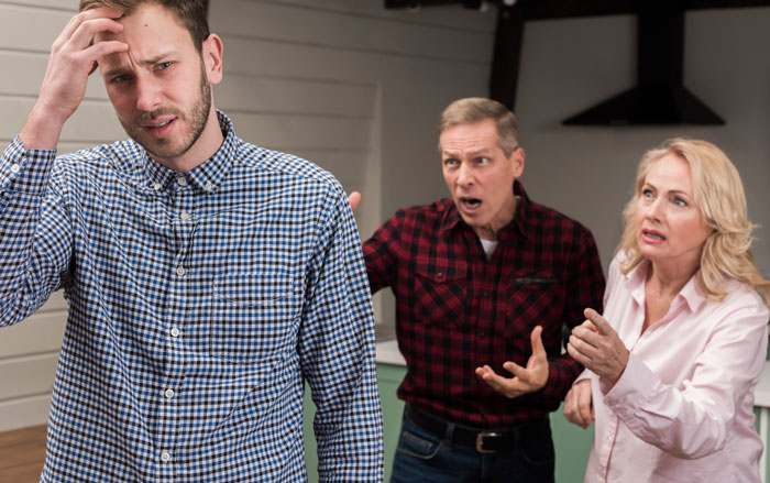 Frustrated young man being scolded by entitled parents who treat autistic brother as golden child ignoring behavior.