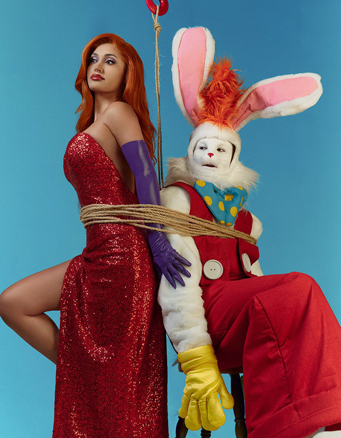 Two celebrities in Halloween costumes with one dressed as a bunny and the other in a red sequined dress tied with rope against blue backdrop