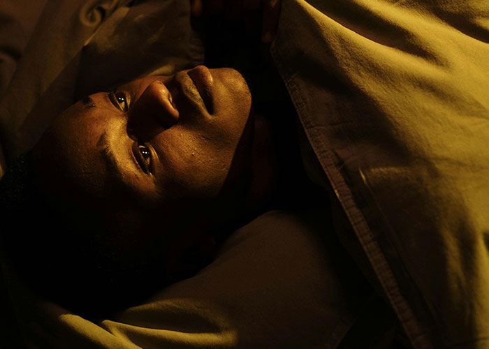 Man lying awake in bed at night, illuminated by dim light, illustrating true stories of bizarre events that creep people out.