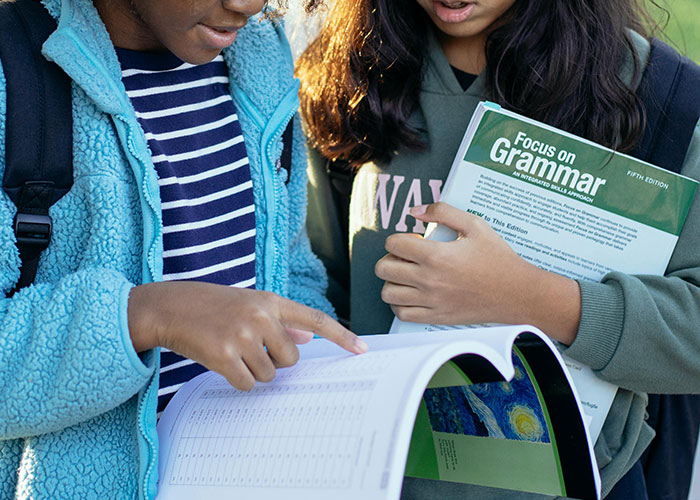 Two students discussing common knowledge while reviewing a grammar book and notes outdoors.